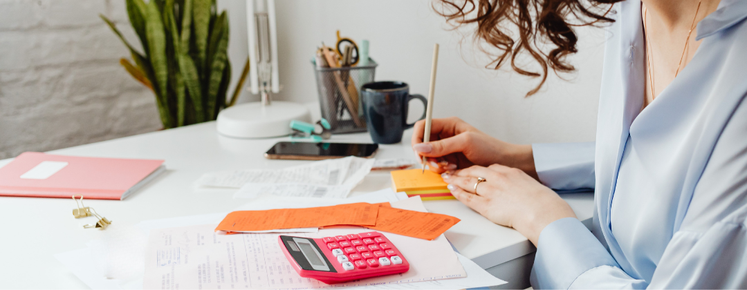 woman at a desk with calculator and papers scattered on desktop.