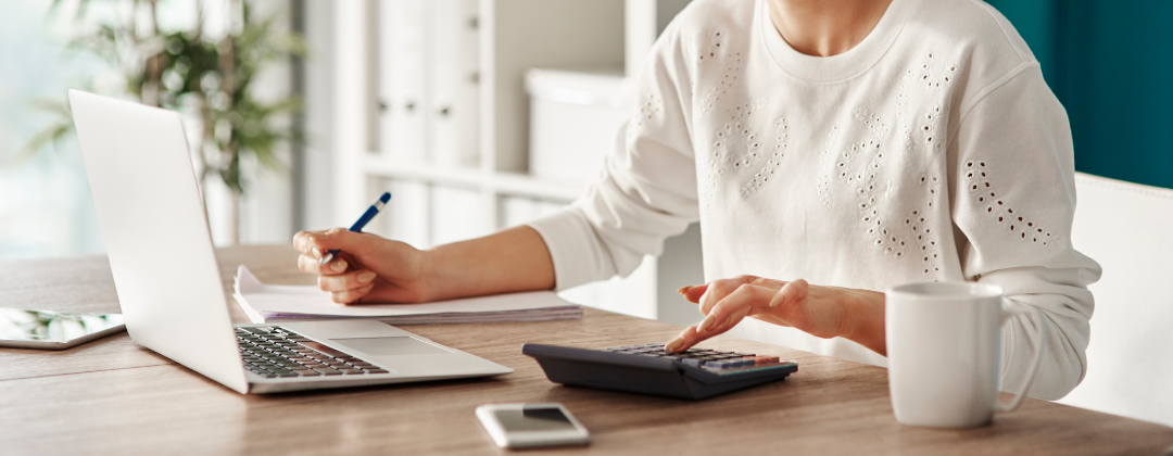 woman at a desk with computer, calculator and coffee cup.